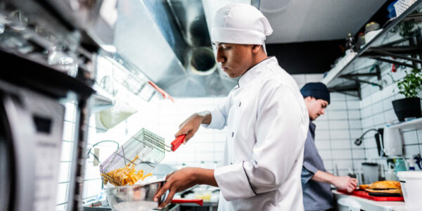 Chef young man making fries on a commercial kitchen