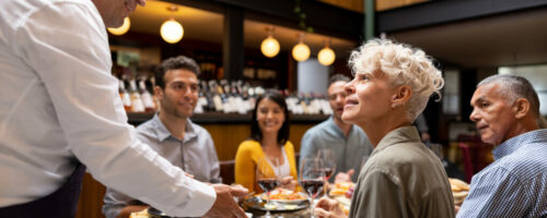 Waiter serving food to a group of friends at a restaurant