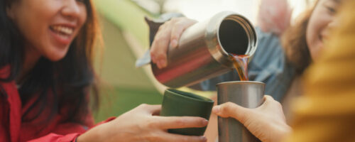 Closeup group of happy Asian friends drinking a cup of hot coffee for breakfast in vacation with camping caravan at morning. Lifestyle travel nature.