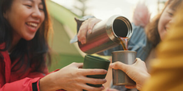 Closeup group of happy Asian friends drinking a cup of hot coffee for breakfast in vacation with camping caravan at morning. Lifestyle travel nature.