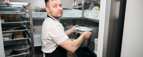 Caucasian male chef putting dish in saucepan on shelf in refrigerator storage