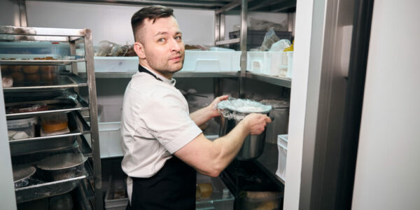 Caucasian male chef putting dish in saucepan on shelf in refrigerator storage