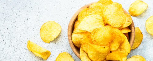 Potato chips in wooden bowl on white table. Top view.