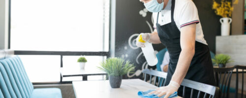 Waiter Spraying Disinfectant On Table